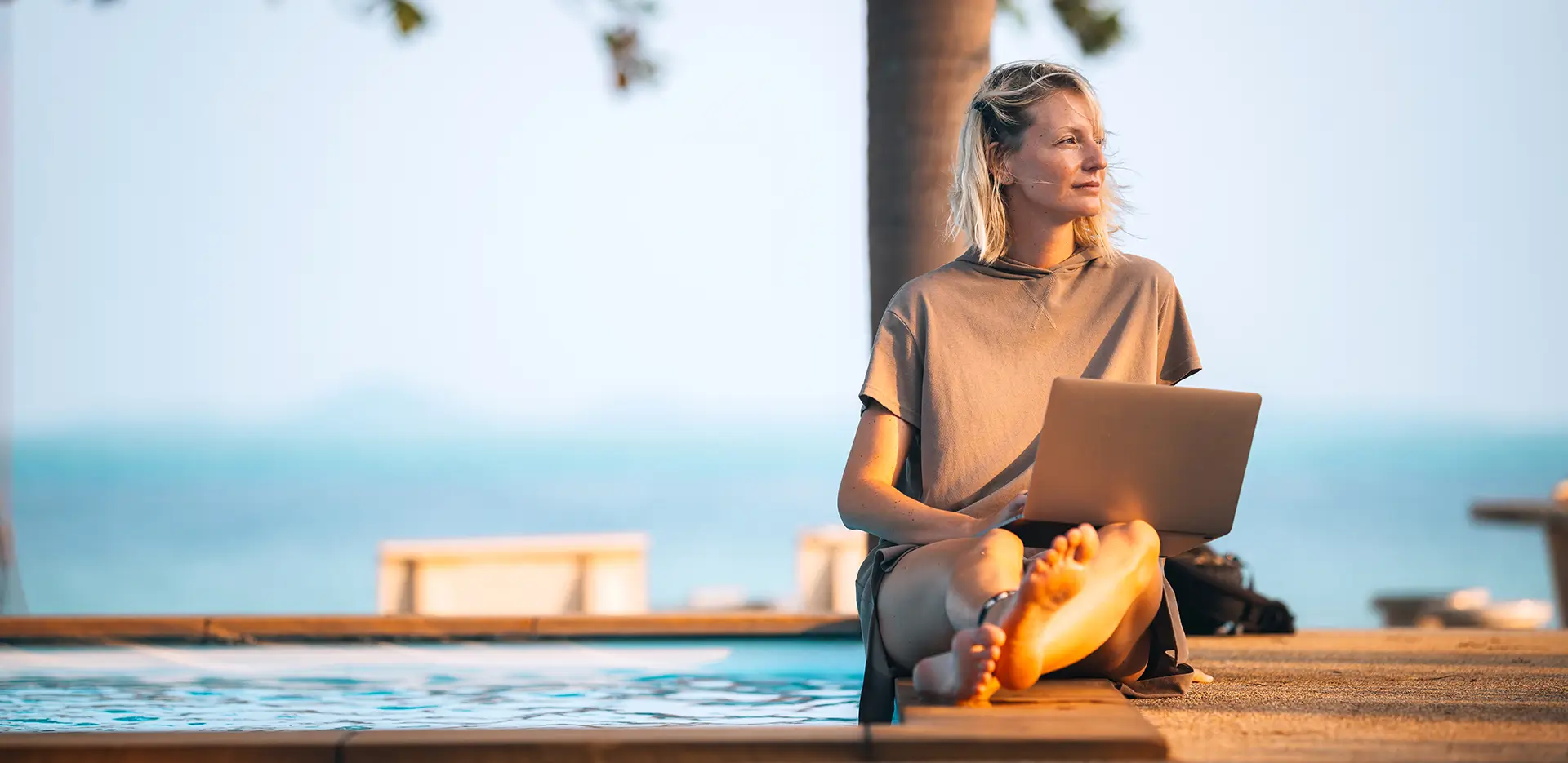 A person sitting beside a pool while working on their laptop computer.