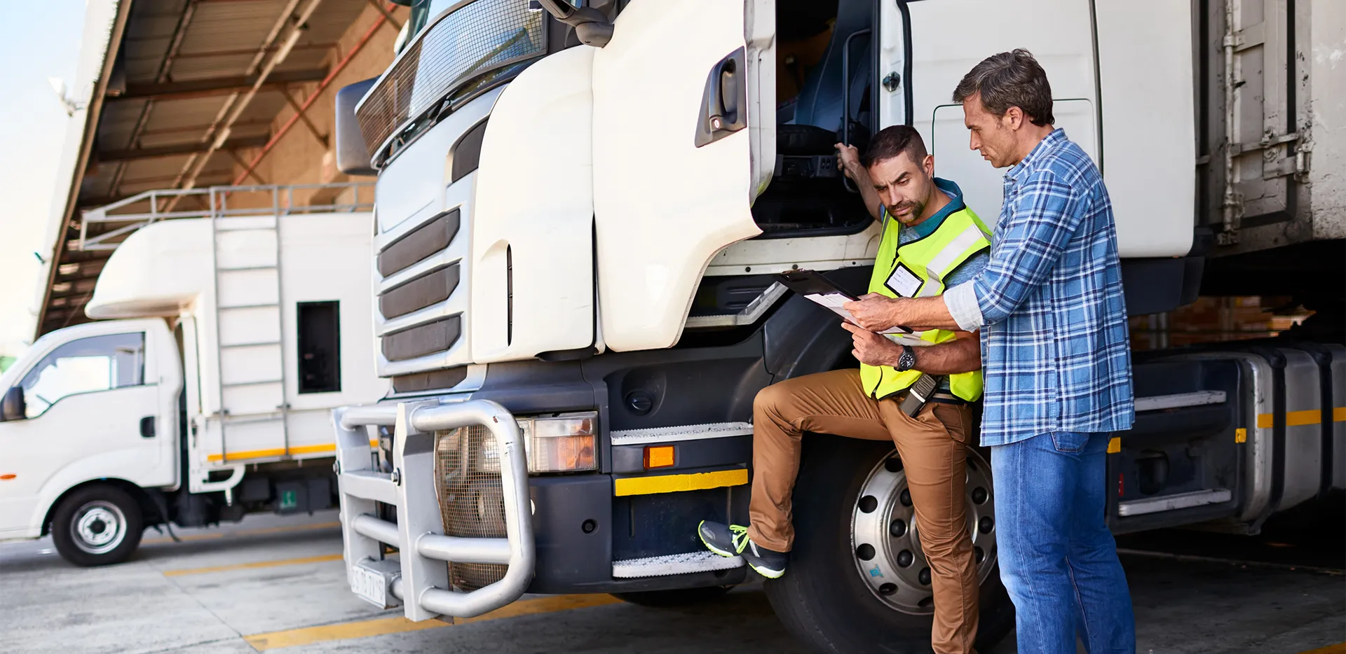 A truck driver speaking with a manager while standing beside their truck.