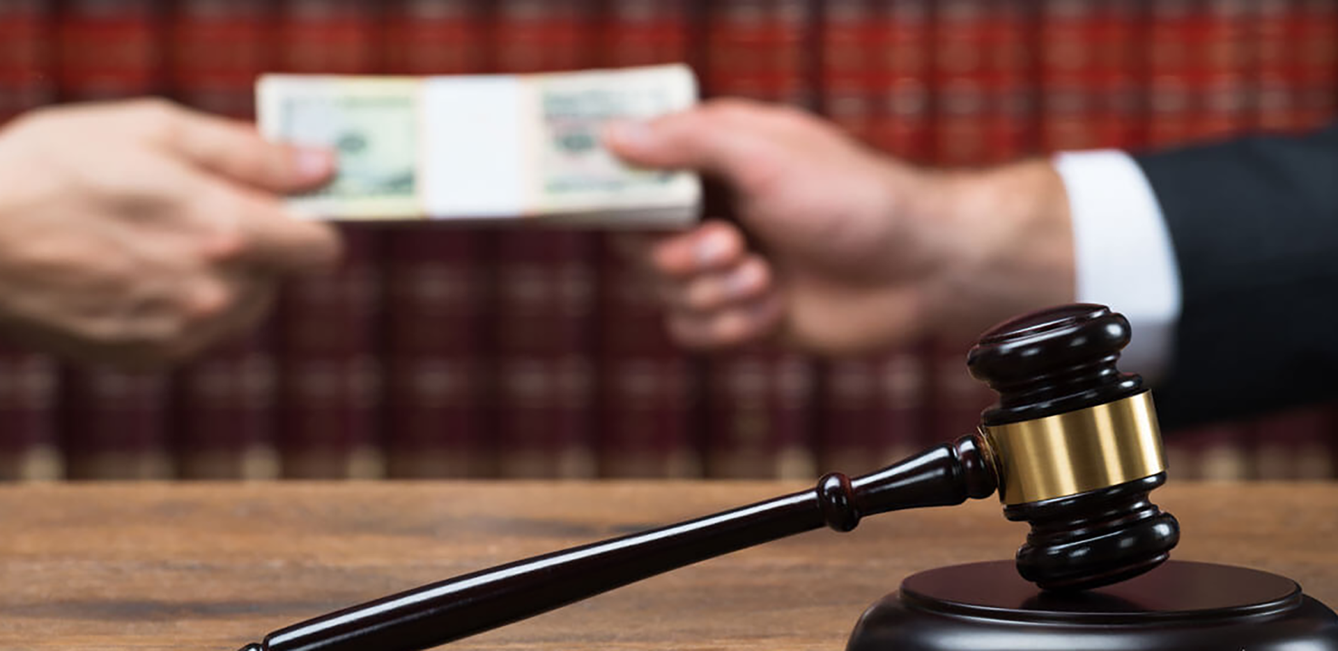 A judge's gavel and sounding block. In the background a stack of money changes hands.