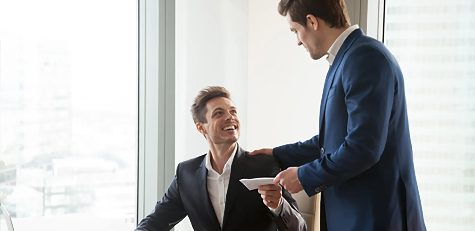 One professional hands paperwork to another while clapping him on the shoulder.
