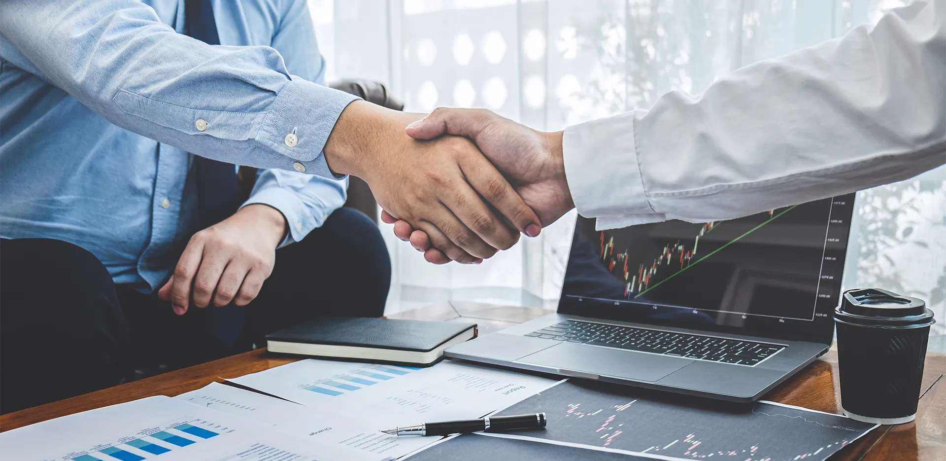 Two people shaking hands in front of a laptop featuring a report.