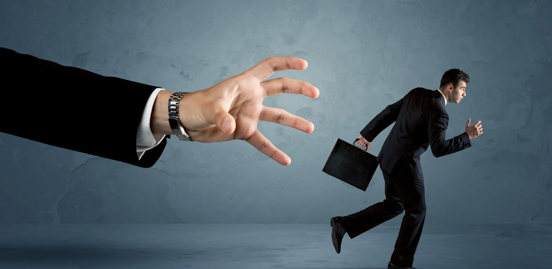 A business man carrying a briefcase and running from a large arm that is reaching out.