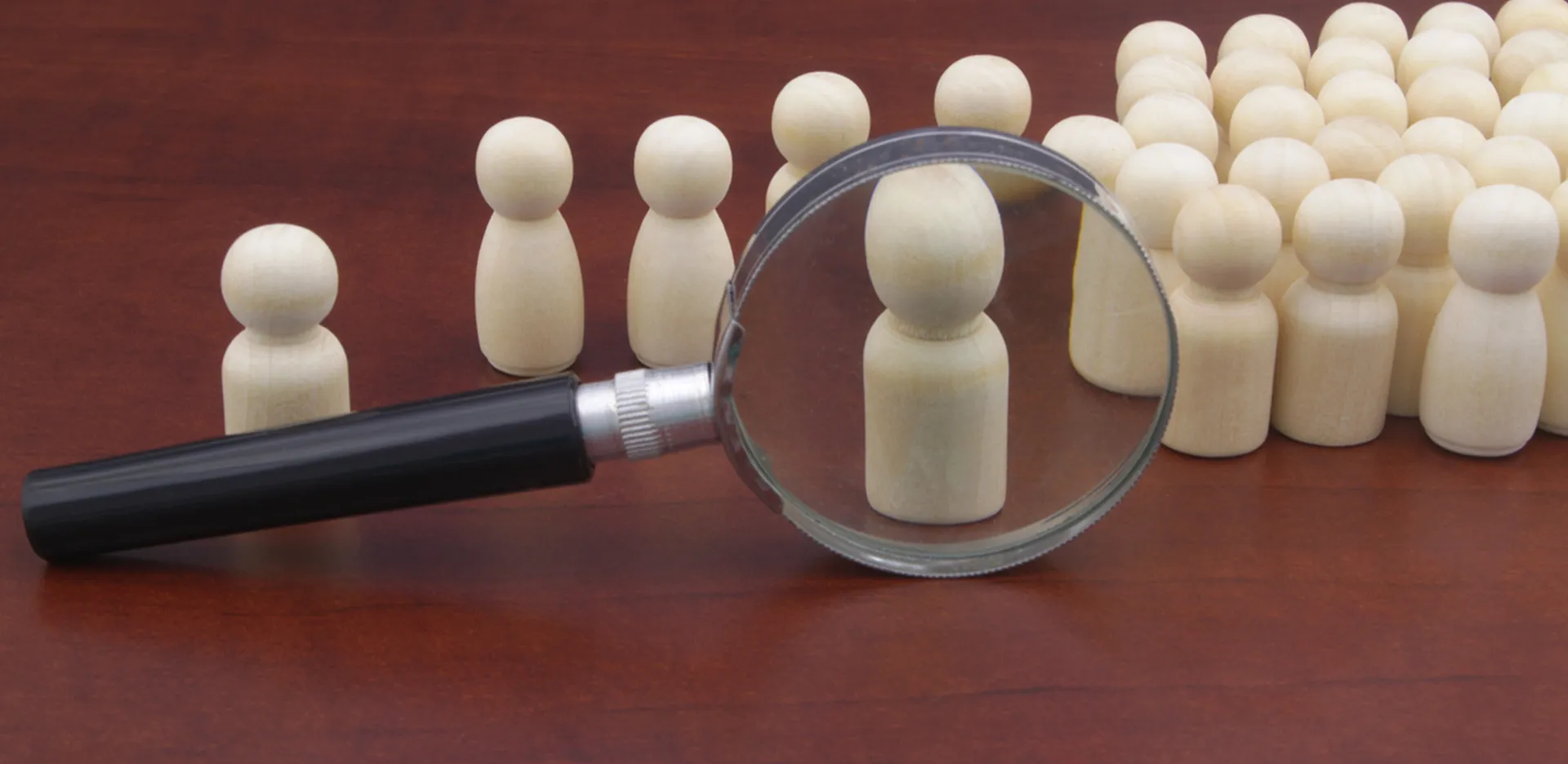 A magnifying glass sitting on a wood surface with chess pawns lined up behind it.