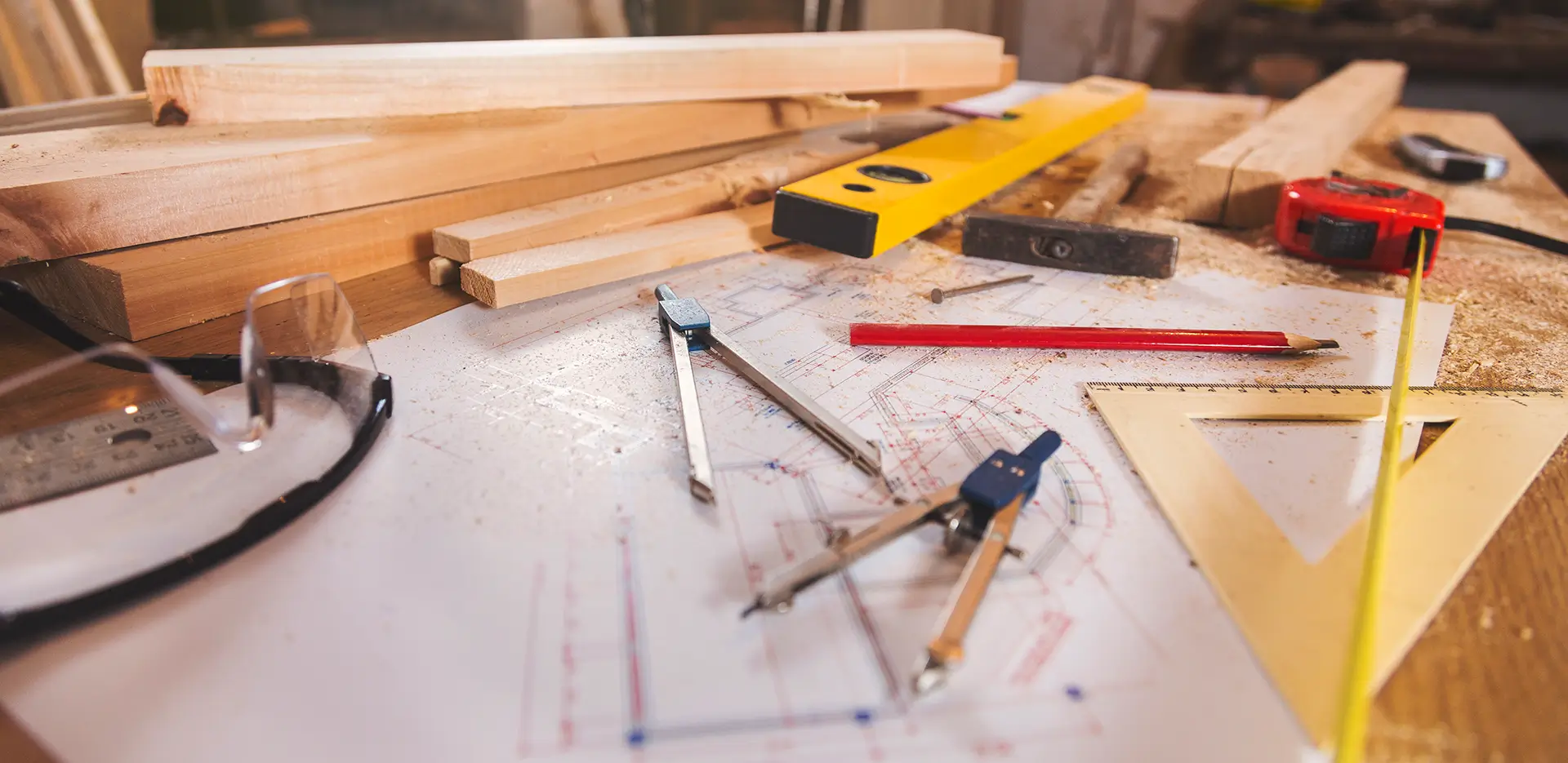 Blueprints coated in sawdust surrounded by lengths of wood and tools.