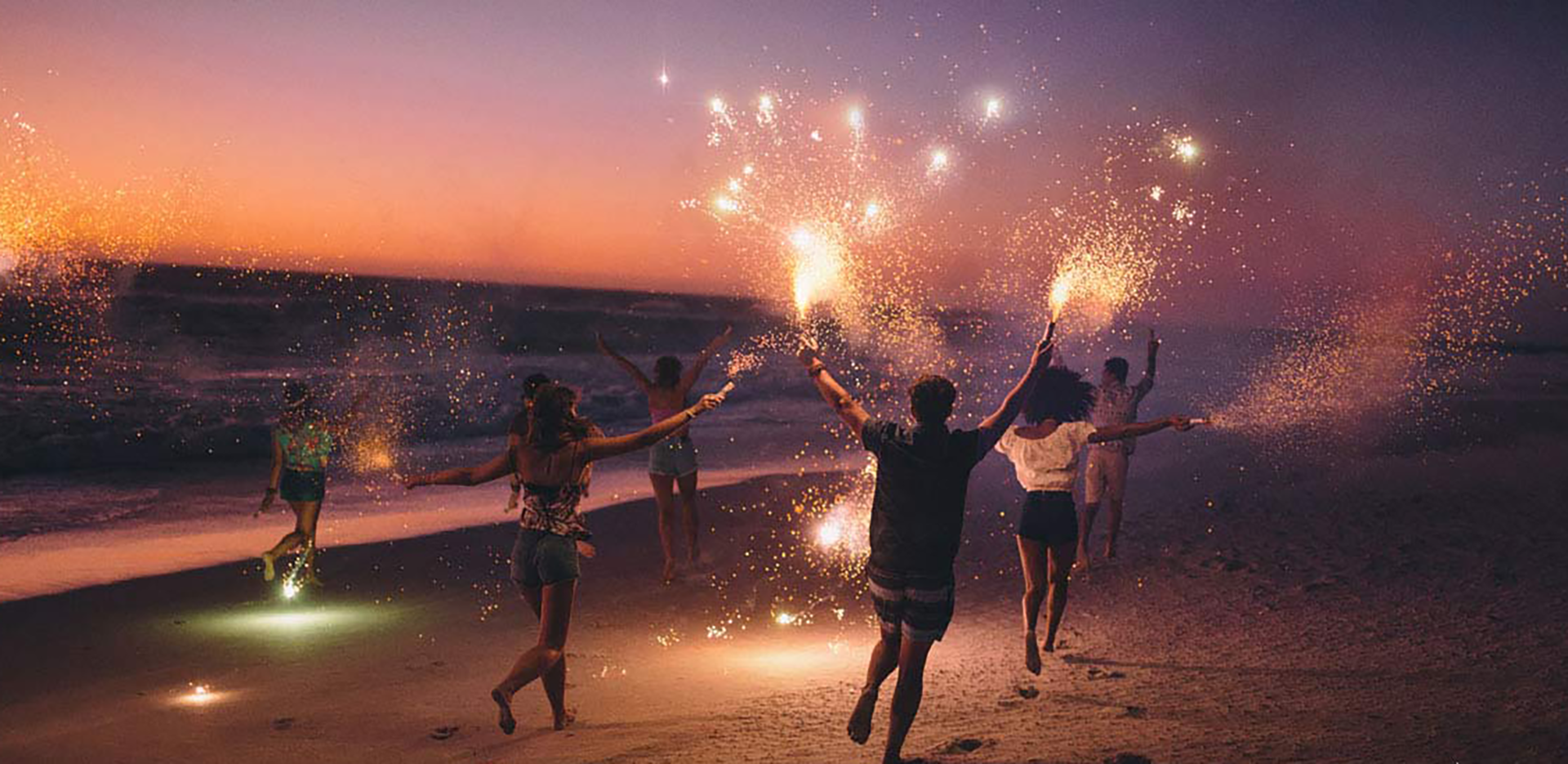 A group of people running down the beach waving sparklers.
