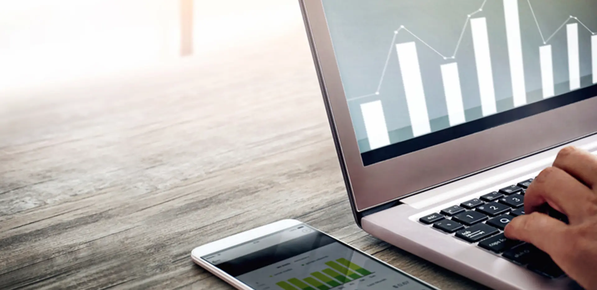 A laptop computer and phone sitting on a desk. Both are displaying bar charts on their screens.