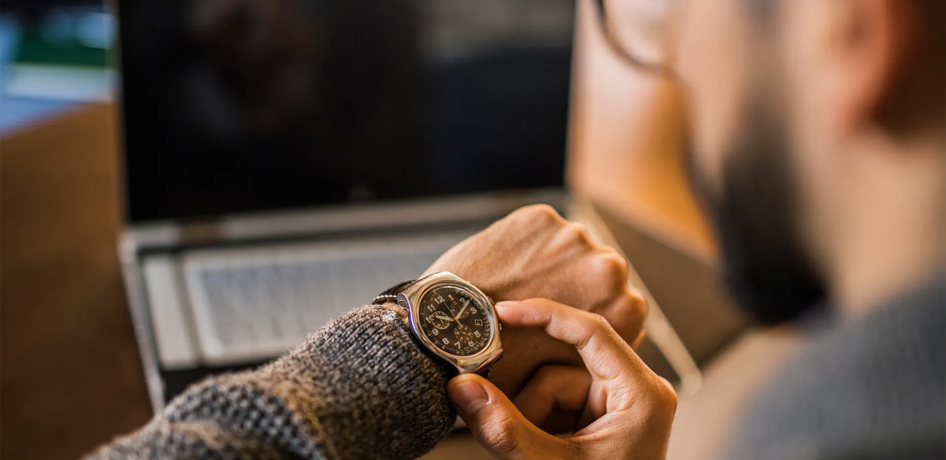 A remote worker looking at their laptop and checking their watch.