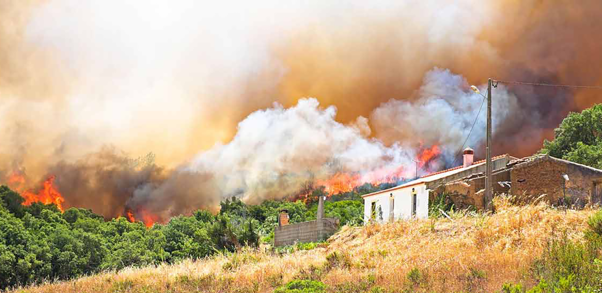 A home on a hillside with a wildfire in the background.