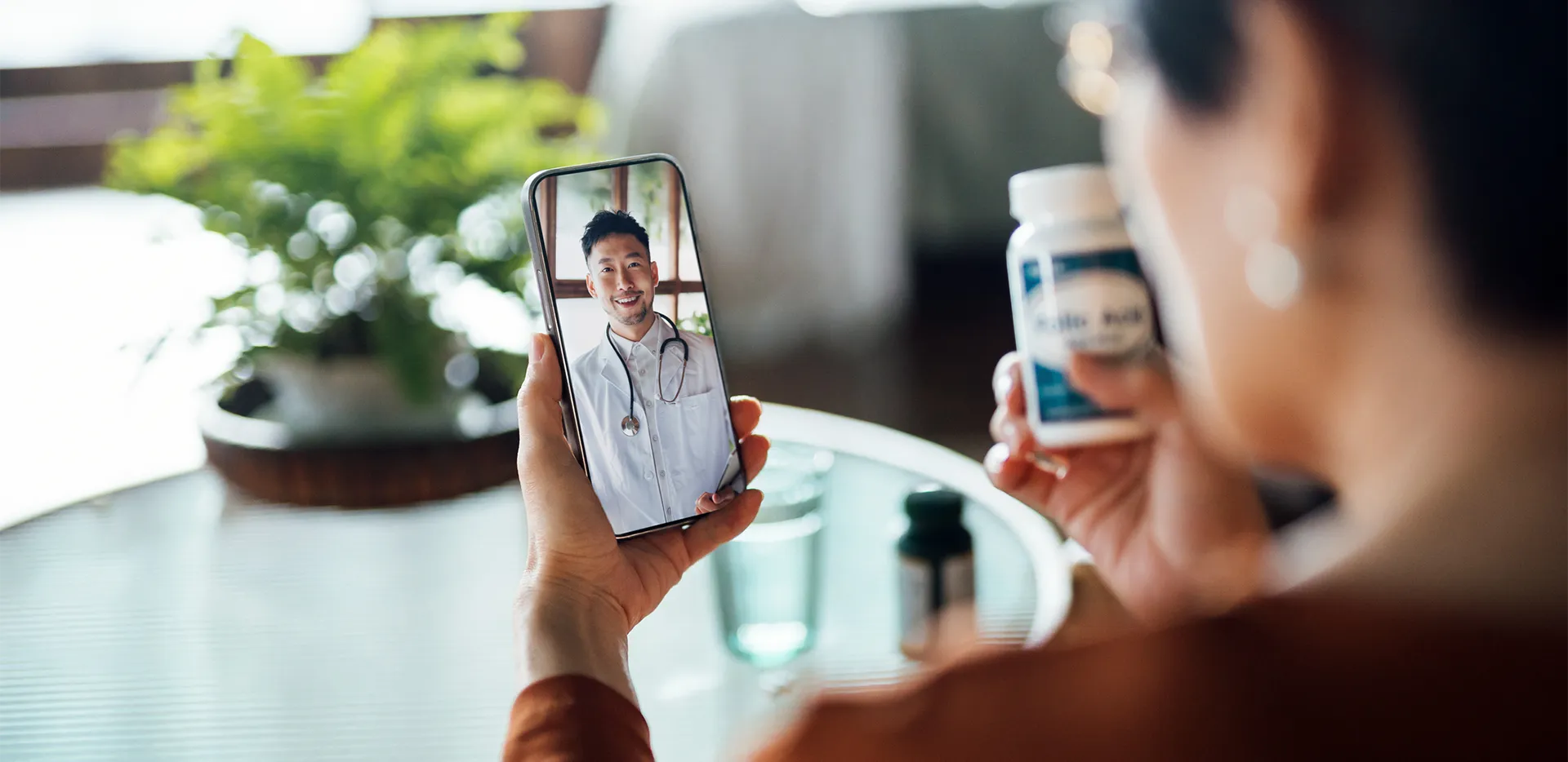 A person on a video call with their doctor, holding a bottle of medication.