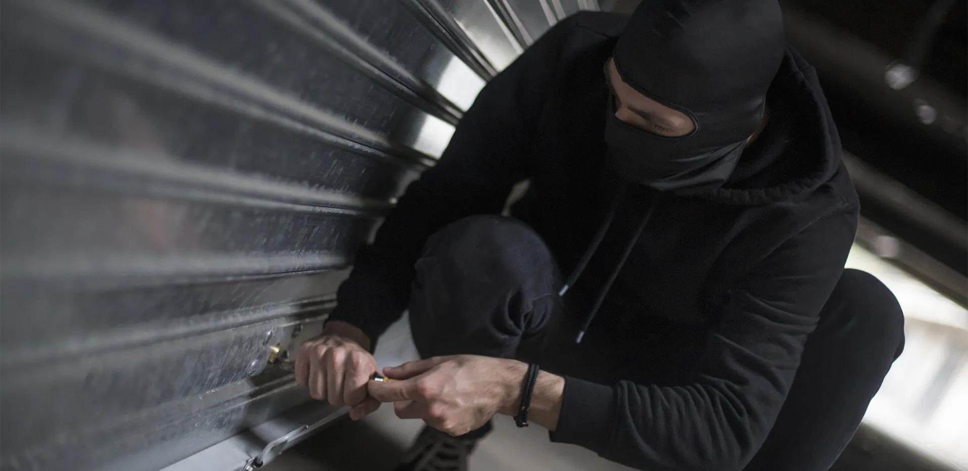 A thief breaking into a silver garage door.