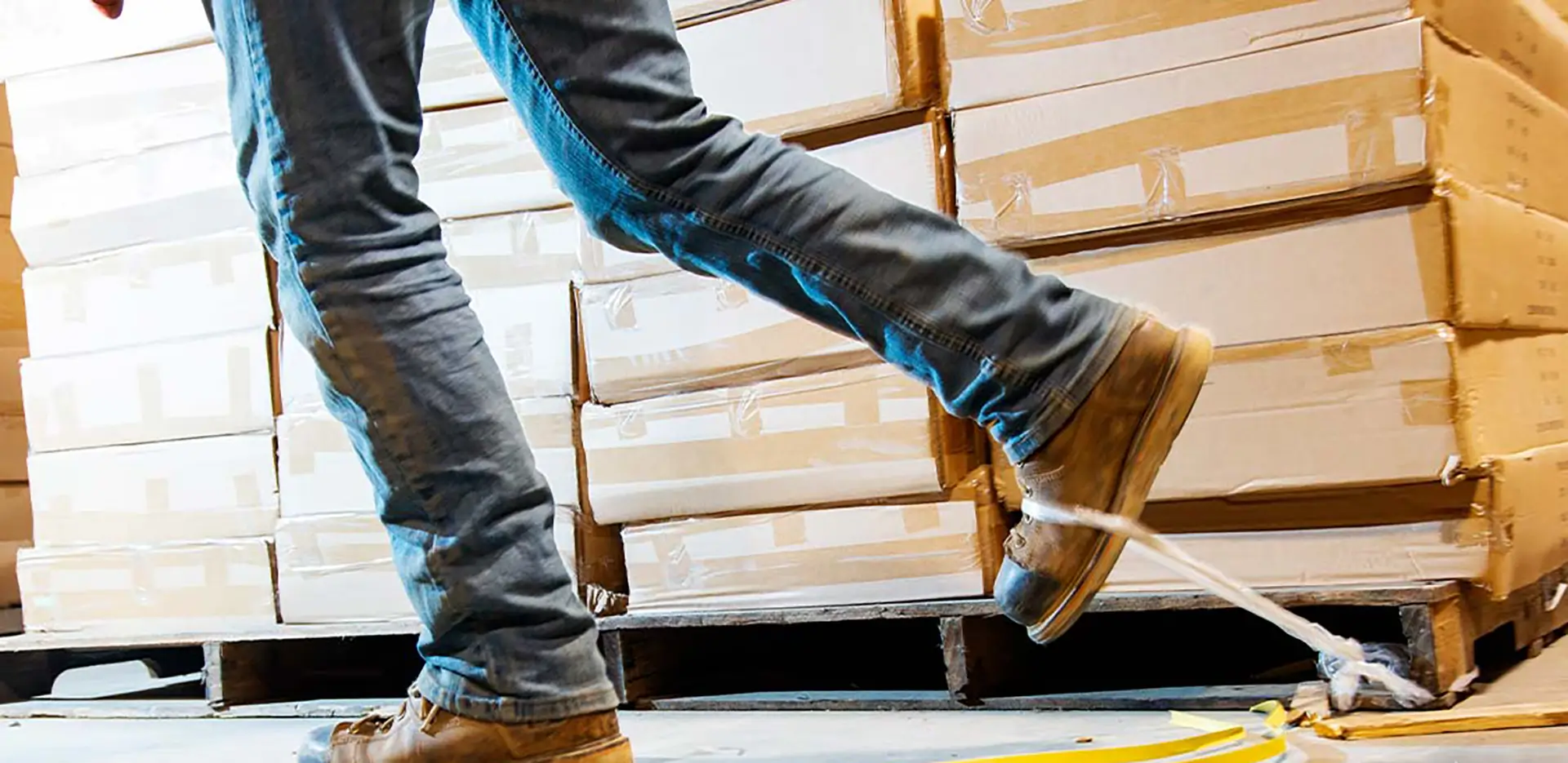 A construction worker tripping over a piece of tape next to a stack of boxes.