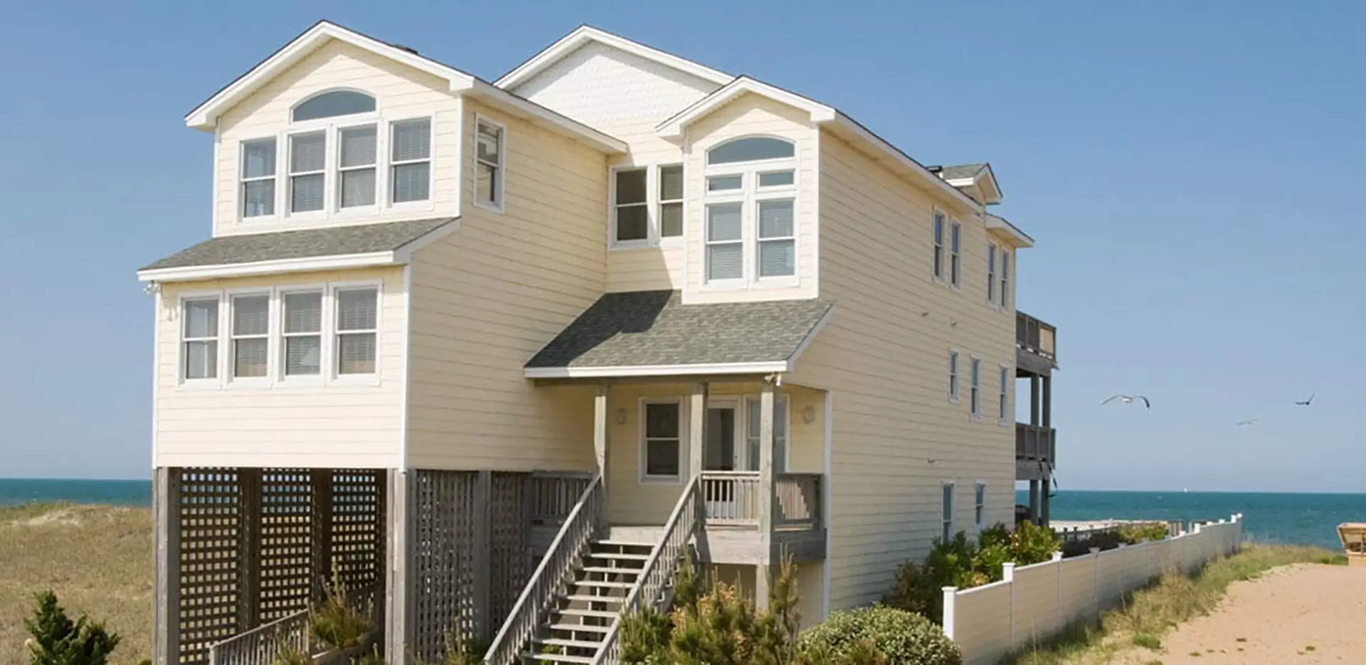 A two story yellow house by the beach.