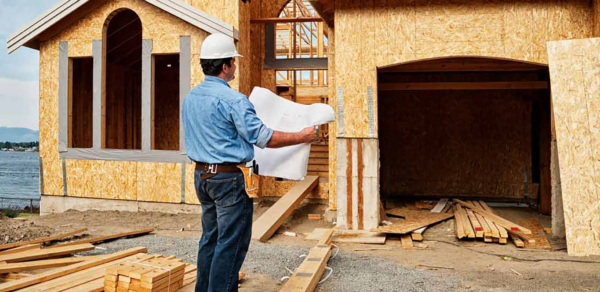 A construction worker standing in front of a house holding blueprints.
