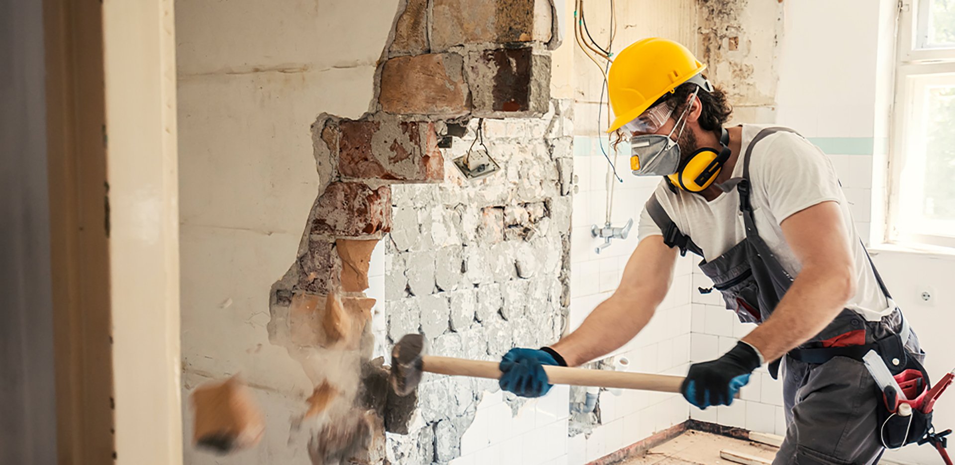 A contractor demolishing a brick wall with a hammer.