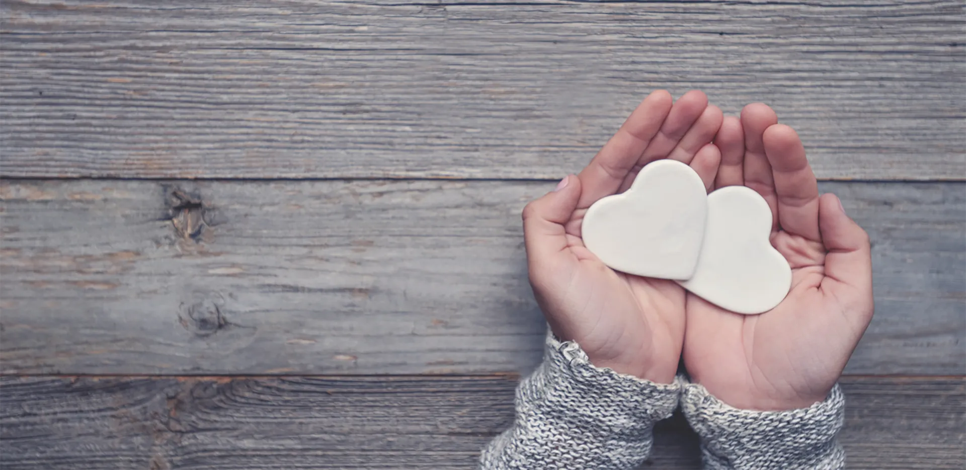 A pair of cupped hands holding two ceramic hearts.