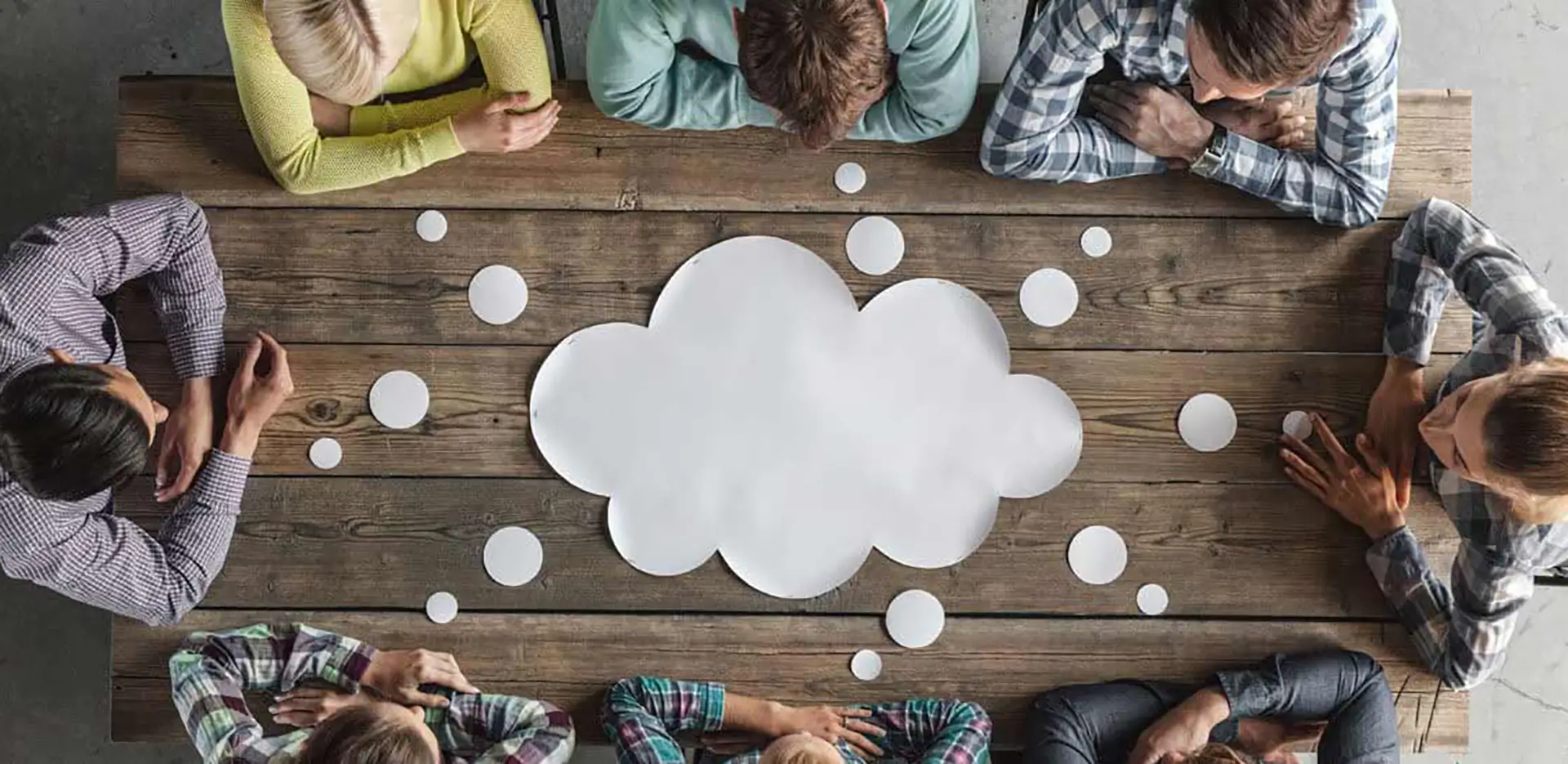 A group of professionals surrounding a table with a paper thought bubble in the middle.