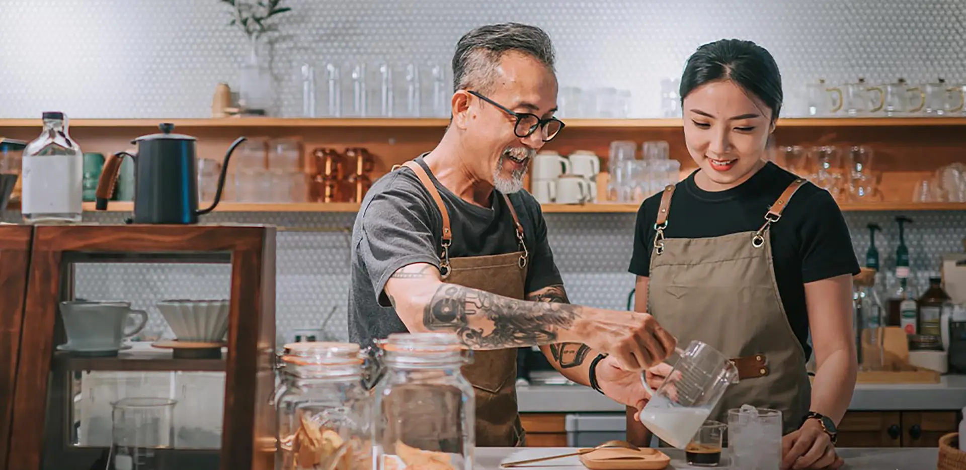 A small business owner teaching an employee how to pour coffee in a cafe.