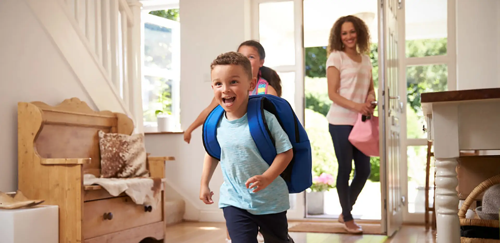 Two children and their mom coming home. The children are wearing backpacks.