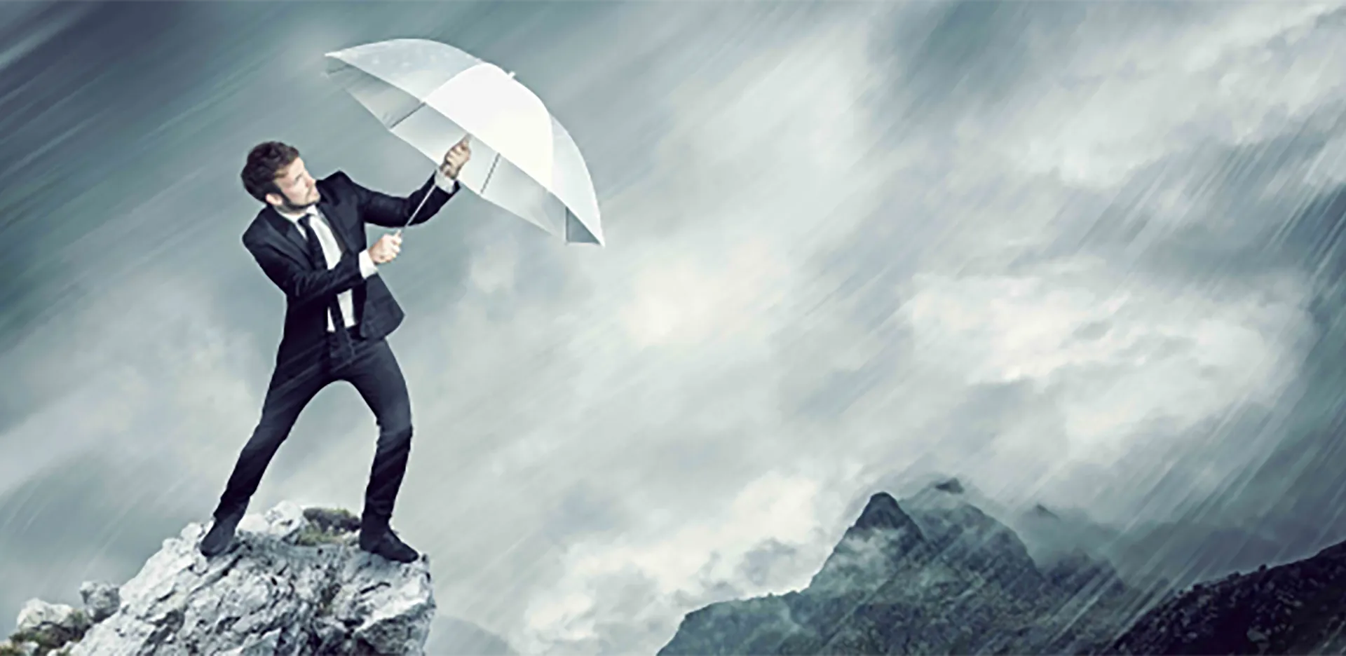 A man wearing a suit holding an umbrella against wind and rain.