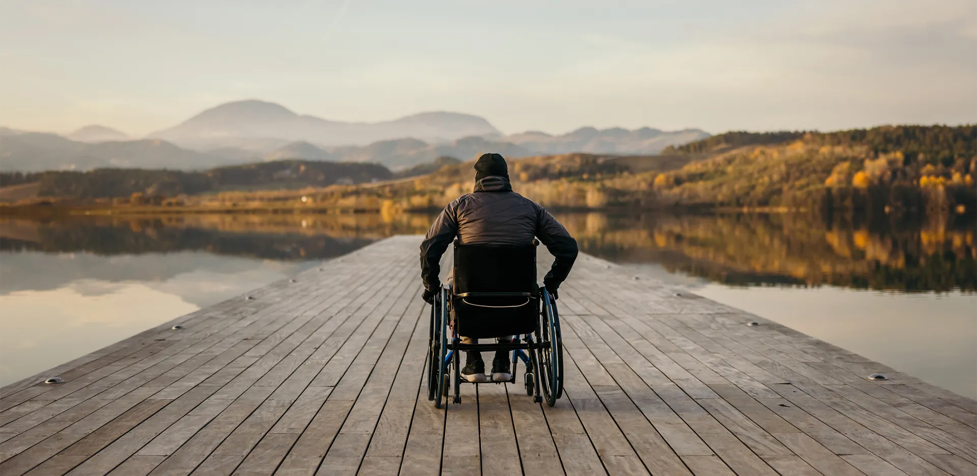 A wheelchair user sitting on a dock looking out at a lake.