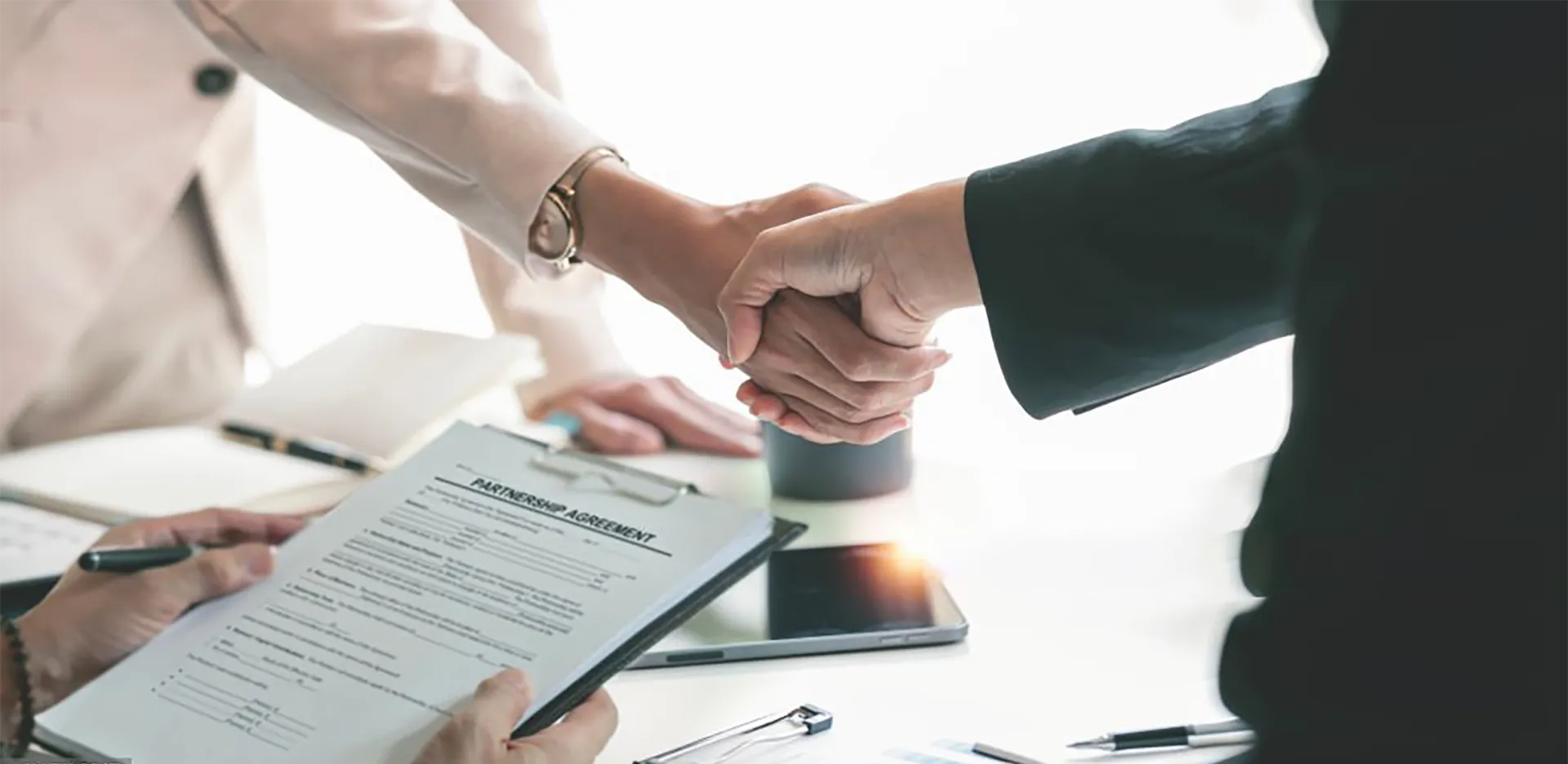 Two professionals shaking hands over a partnership agreement.
