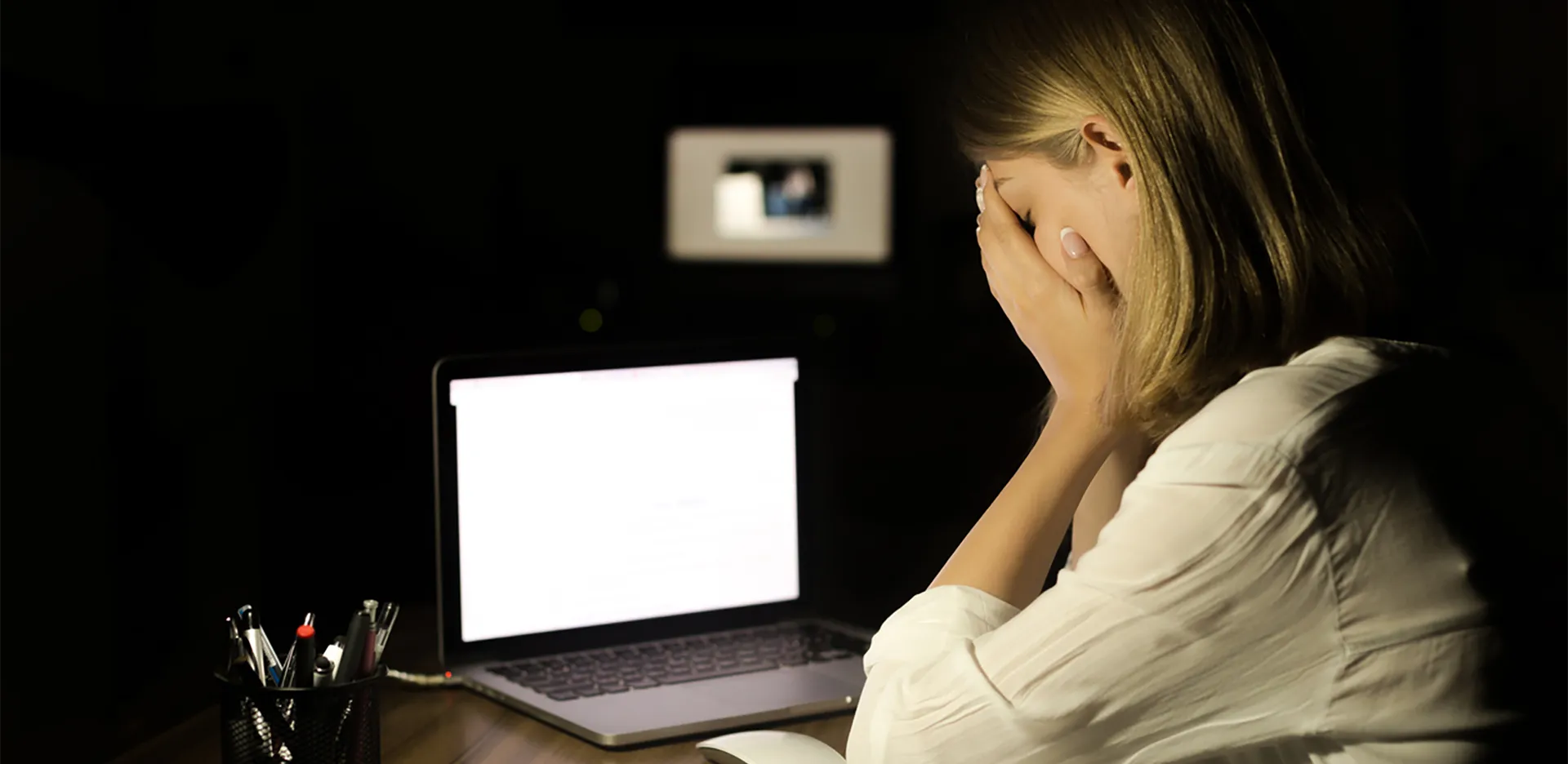 A woman looking with frustration at a laptop computer in a dark room.
