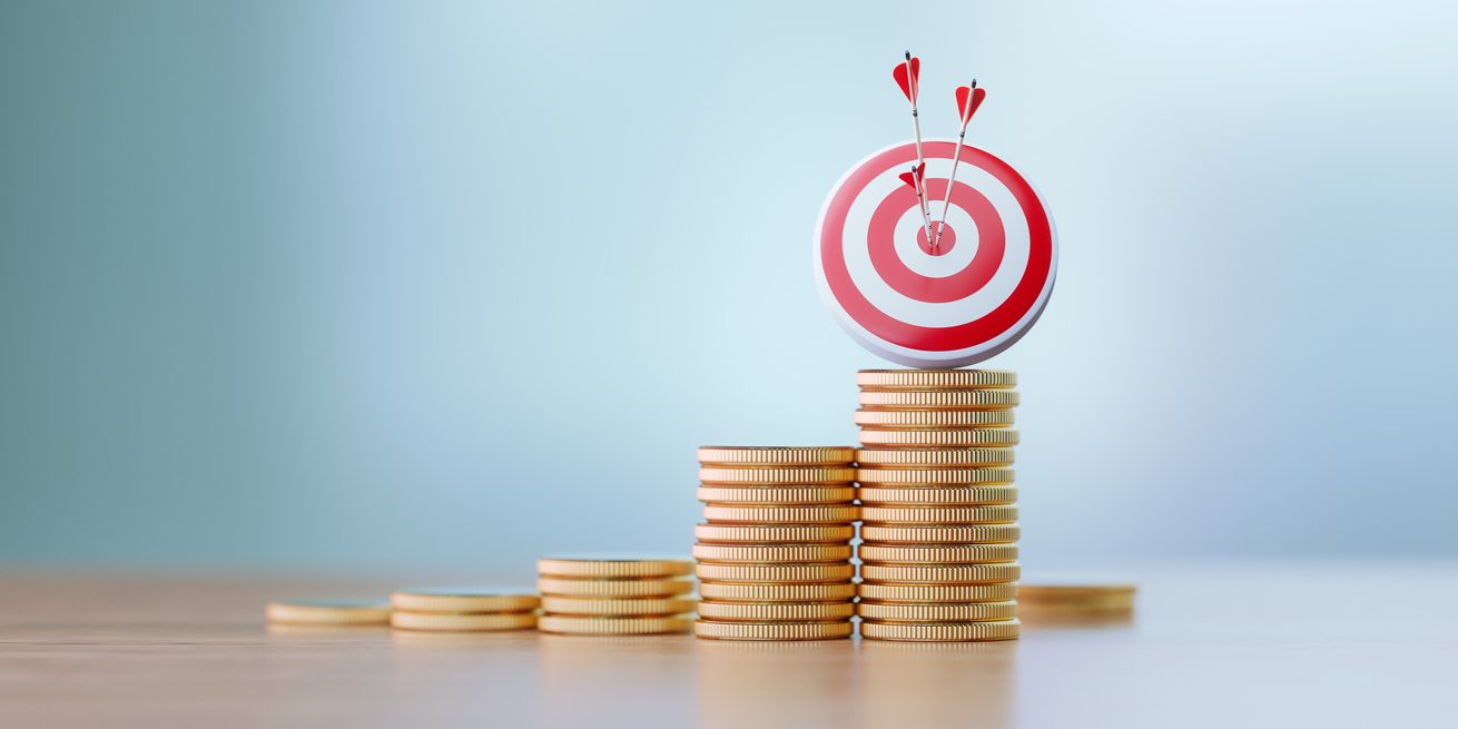 Red dartboard and arrows sitting over coin stacks before defocused background. Horizontal composition with copy space. Success and accuracy concept.