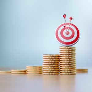 Red dartboard and arrows sitting over coin stacks before defocused background. Horizontal composition with copy space. Success and accuracy concept.