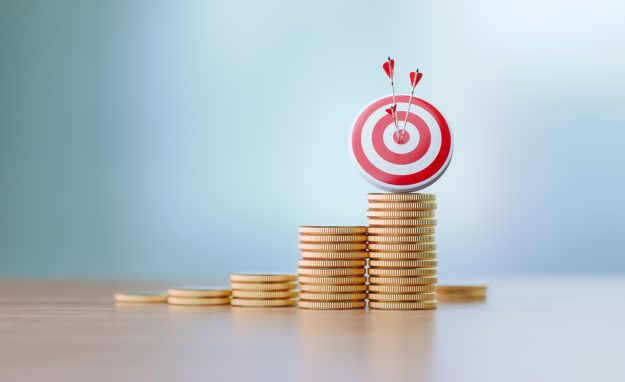 Red dartboard and arrows sitting over coin stacks before defocused background. Horizontal composition with copy space. Success and accuracy concept.