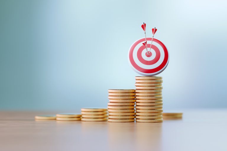 Red dartboard and arrows sitting over coin stacks before defocused background. Horizontal composition with copy space. Success and accuracy concept.