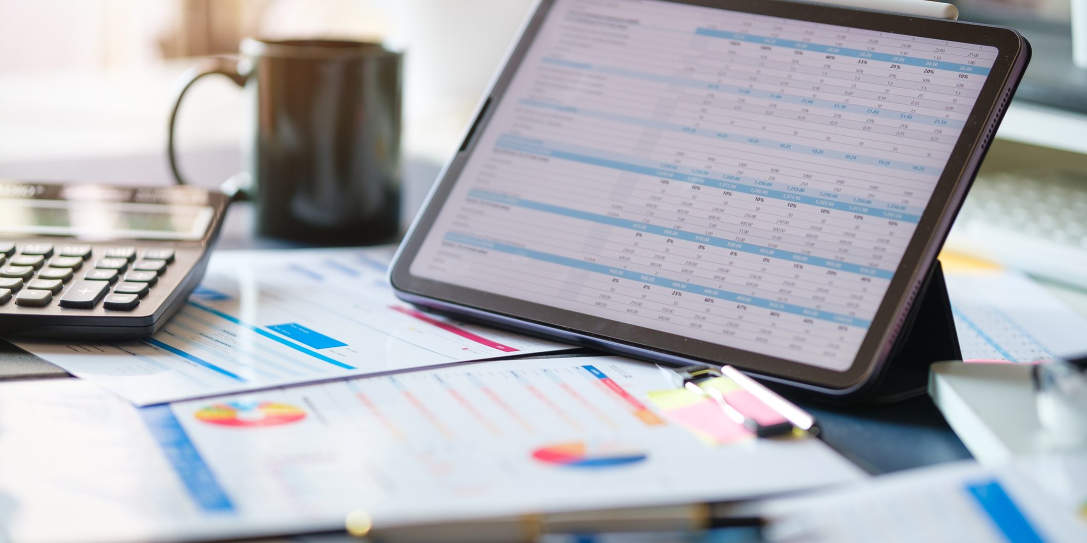 Digital tablet with profit and tables on screen, calculator, financial reports on wooden desk.