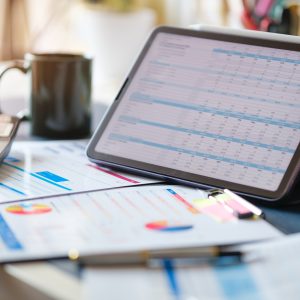 Digital tablet with profit and tables on screen, calculator, financial reports on wooden desk.