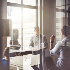 A photo of business people having discussion in board room. Male and female professionals are seen through glass. They are working in office.