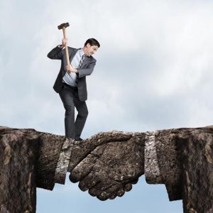 A businessman swings a sledgehammer at a land bridge connecting two cliffs as he tries to chip away at the metaphorical agreement represented by the bridge formed in the shape of a handshake.