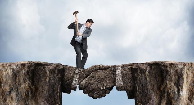 A businessman swings a sledgehammer at a land bridge connecting two cliffs as he tries to chip away at the metaphorical agreement represented by the bridge formed in the shape of a handshake.